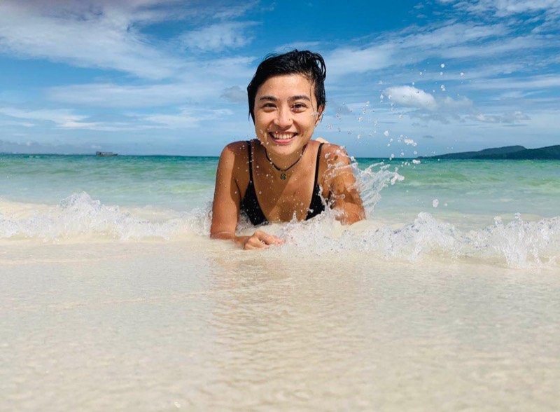 Una persona sonriente tumbada en la orilla de una playa luminosa.