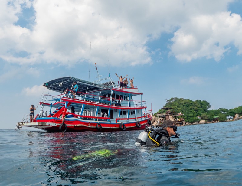El barco rojo de buceo Rungworawan con buceadores en el agua a su lado.