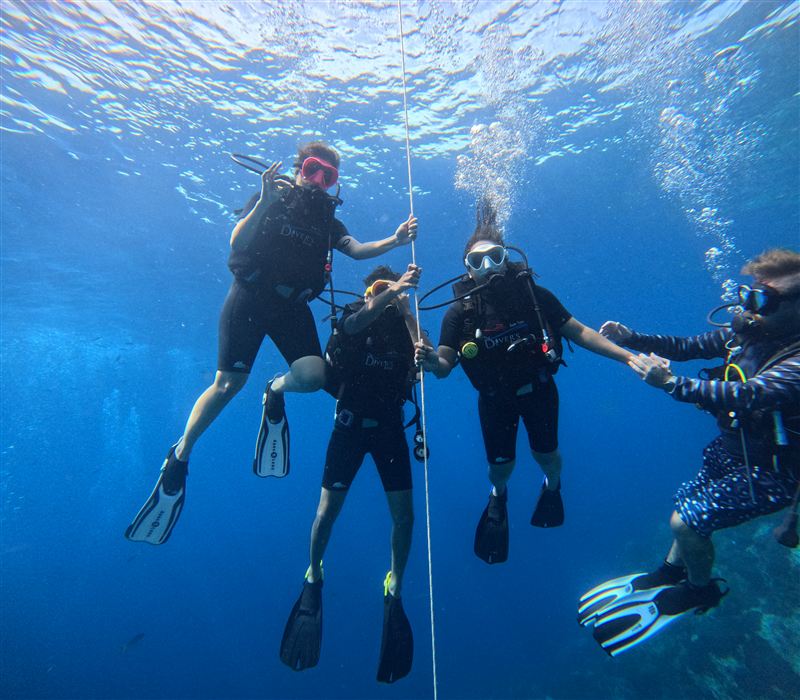 Tres alumnos de bautismo agarrados al cabo de descenso en agua azul y clara mientras su instructor los guía.