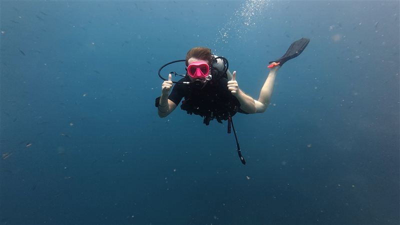 Un buceador con máscara rosa levantando los dos pulgares en el azul profundo.